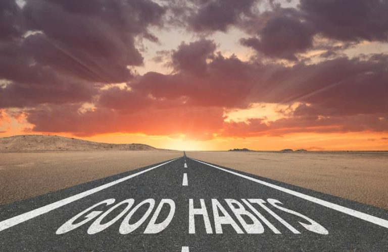 A long straight road in the middle of a barren desert leading off into a very colourful sunset. At the start of the road are the words "good habits" painted on it.