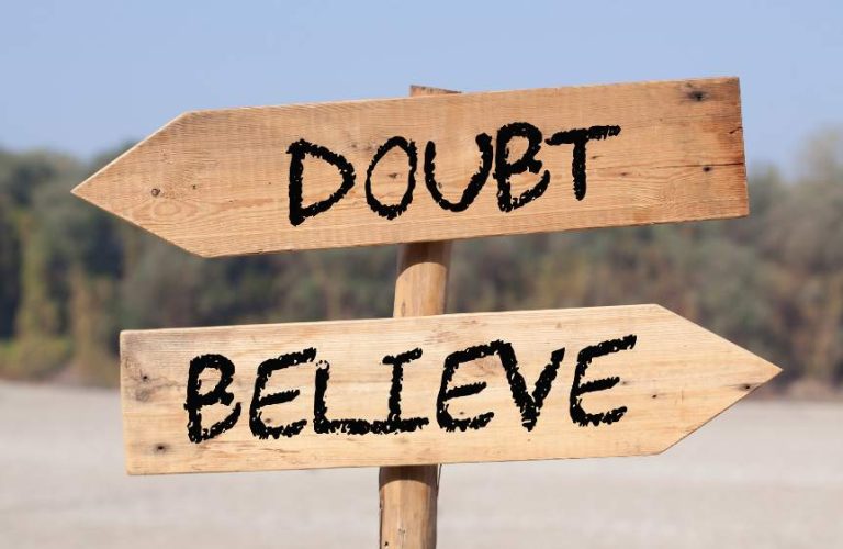 A wooden sign post with two wooden arrows pointing in different directions. One says doubt and the other says believe.